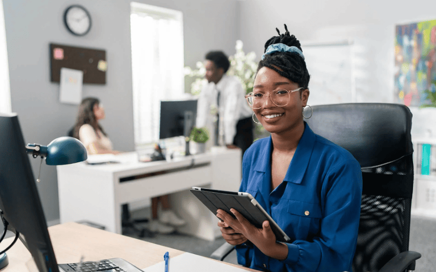 Mulher trabalhando em escritório de contabilidade com tablet na mão e computador à frente