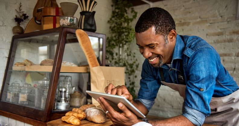 Rapaz em sua padaria com várias fornadas de pães ao fundo