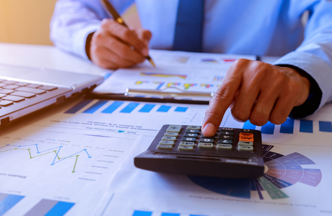 Mão fazendo contas com caneta e calculadora representando regimes tributários no Brasil