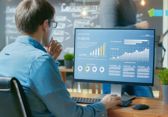 Rapaz trabalhando em escritório financeiro de frente para o computador, representando análise de dados e gestão financeira