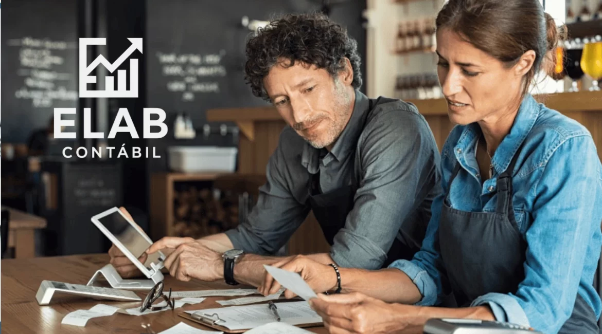 Homem e mulher sentados à mesa usando notebook e fazendo contas para organizar as finanças da empresa