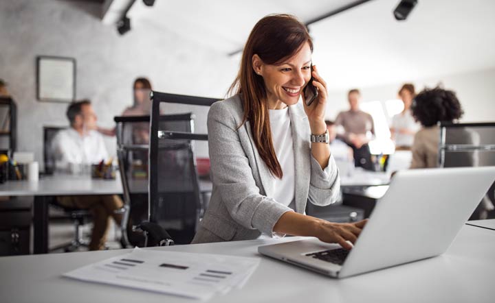 Mulher trabalhando no escritório com notebook e telefone ao ouvido, realizando atividades profissionais