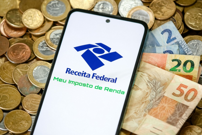 Celular com aplicativo da Receita Federal exibindo pagamento de impostos e notas de reais ao redor.