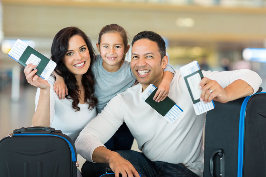 Família feliz caminhando com malas no aeroporto pronta para viajar.